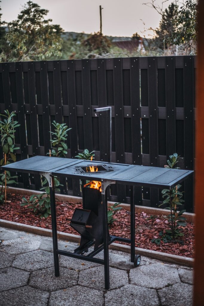 Lézervágott ARKVIK kerti tűzrakó grillasztal a kertben, kerekekkel